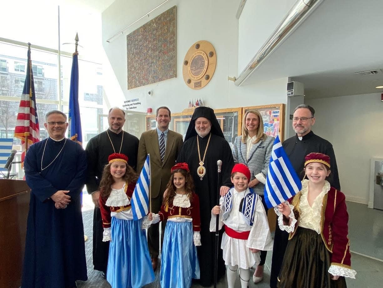 Mayor Simmons with Greek Orthodox Archbishop Elpidophoros, Congressman Himes, Members of the Clergy, and Children smile for a photo at greek independence day celebration